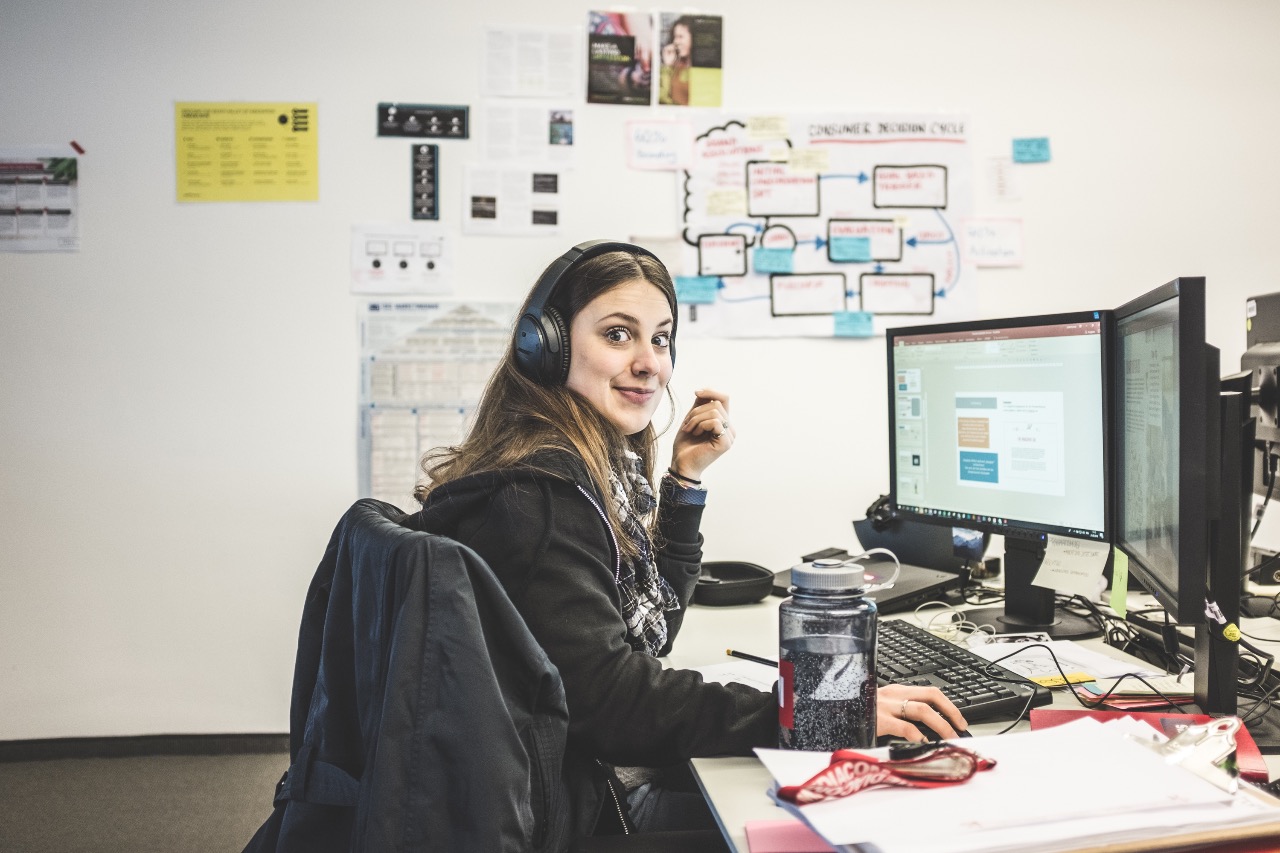 Judith in der Mediaagentur, am Schreibtisch mit Headphones